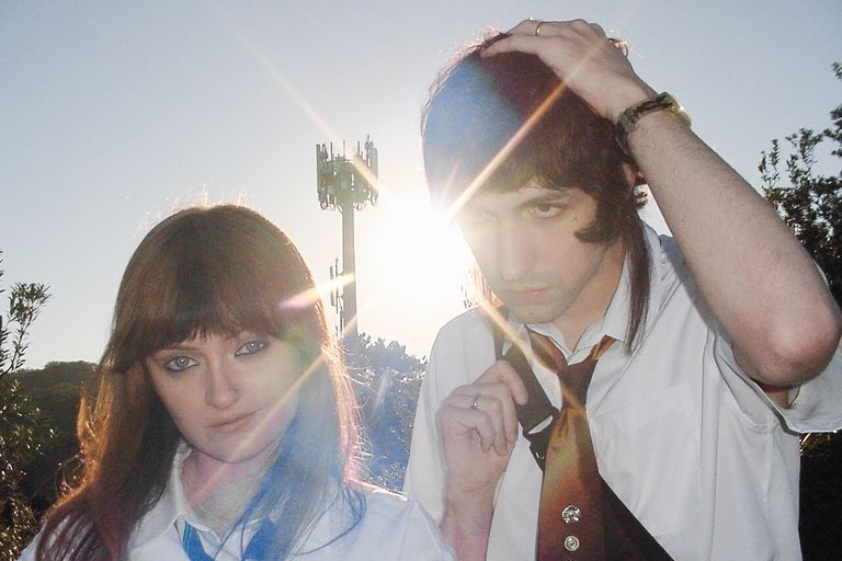 Electronic music producers Ninajirachi and Porter Robinson posing together in white collared shirts in a lens-flared outdoor promotional photo.